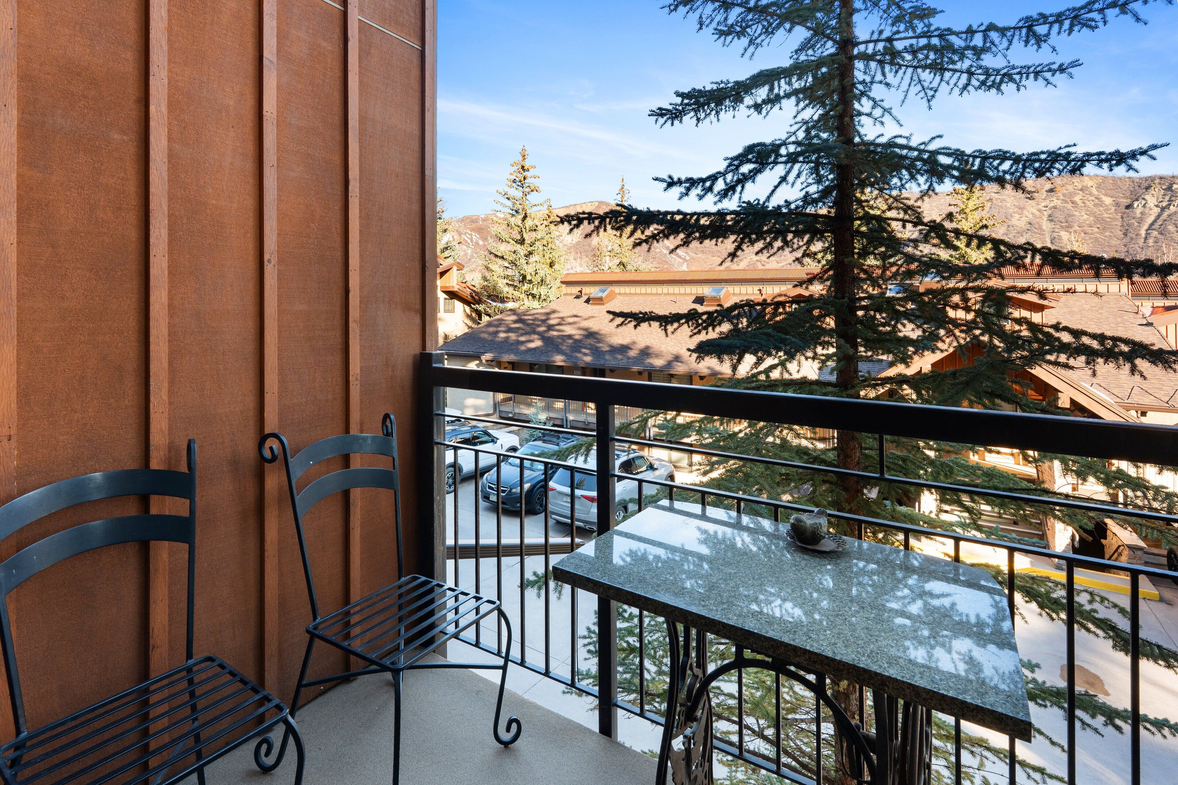 A balcony with a table and chairs, overlooking a parking area and a mountainous landscape.
