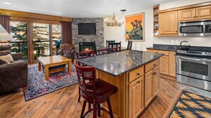 A spacious living area with a fireplace, a dining table, and a kitchen with modern appliances. - Crestwood 2109 Premier 2 Bedroom (Snowmass Village)