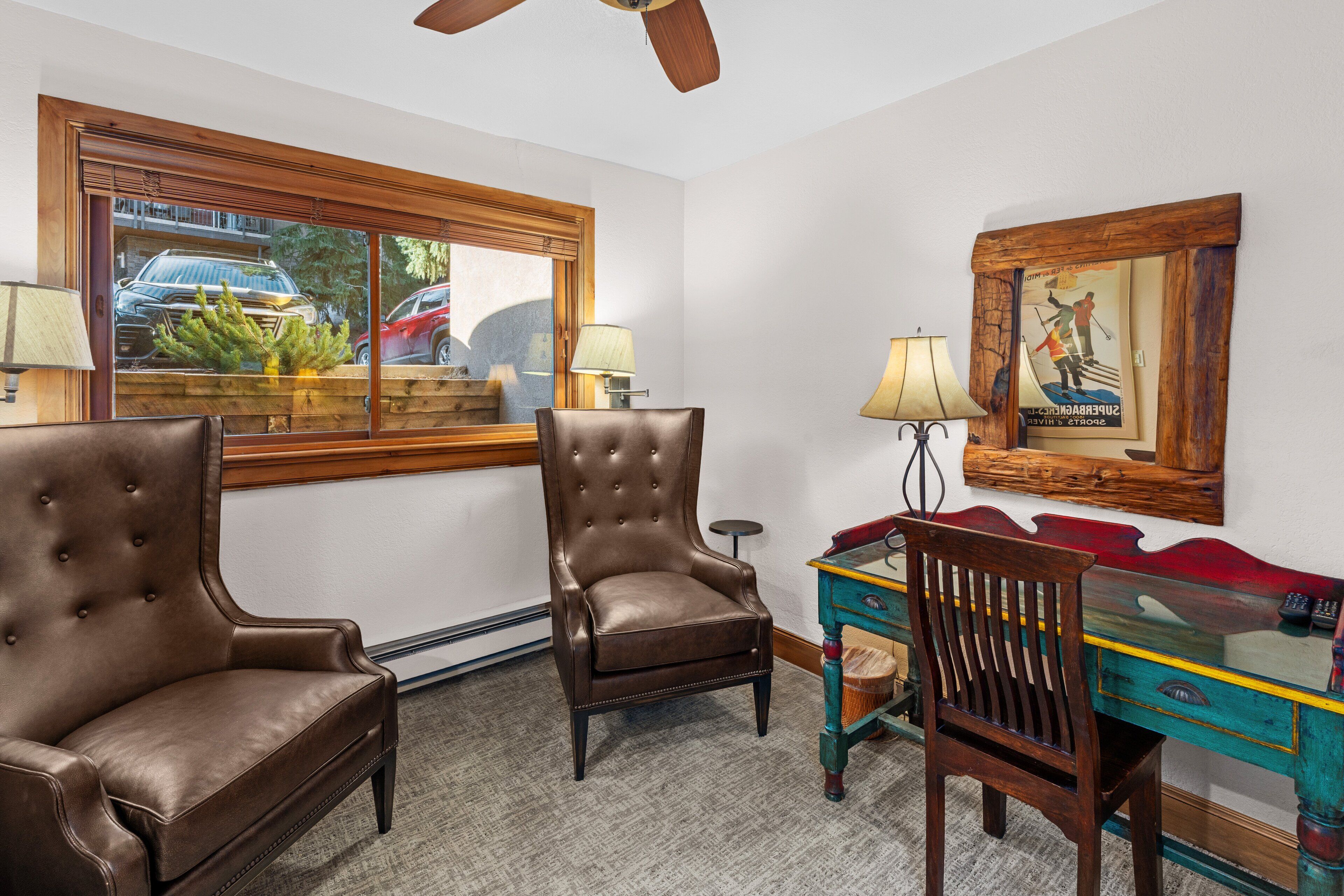 A room with two leather armchairs, a wooden desk, and a large window with a view of parked cars.