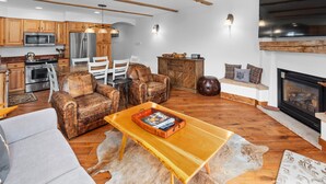A spacious living area with a fireplace, wooden furniture, and a kitchen in the background.