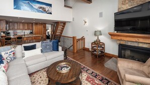 Un salón amplio con chimenea, un televisor de pantalla plana grande y una cocina al fondo.