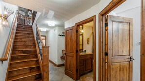Una escalera de madera que lleva a un baño con lavamanos y espejo.