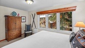 Ein Schlafzimmer mit einem großen Bett, einer Holzkommode, einem Stuhl und einem Fenster mit Blick auf ein Gebäude und Bäume.