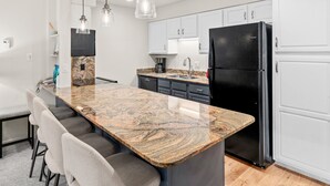A modern kitchen with a granite countertop, white cabinets, and a black refrigerator.