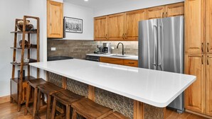 A modern kitchen with wooden cabinets, a stainless steel refrigerator, a white countertop, and a built-in bench.