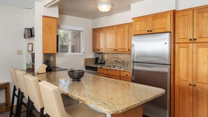 A kitchen with granite countertops, wooden cabinets, a stainless steel refrigerator, and a built-in island with bar stools. - Crestwood 2117 Standard 2 Bedroom (Snowmass Village)