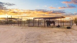 A stable with a horse inside, surrounded by a metal fence and a covered shelter.