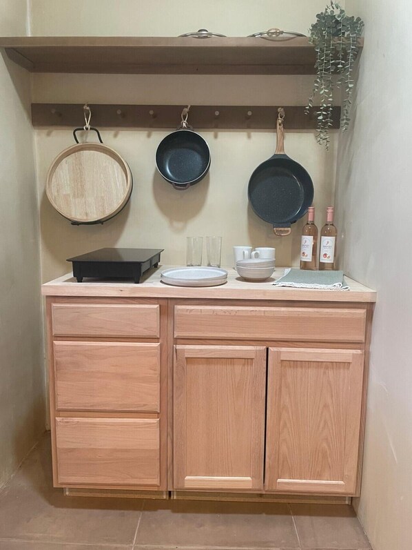 A kitchen with wooden cabinets, a countertop, hanging pots, glasses, and bottles.