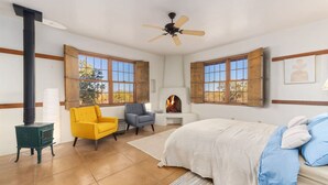 A bedroom with a bed, two chairs, a fireplace, and a ceiling fan.