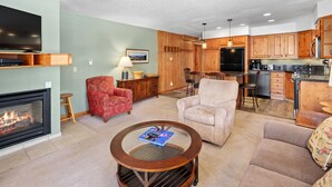 A living room with a fireplace, a round coffee table, and a television. - Crestwood 2101 Deluxe 2 Bedroom (Snowmass Village)