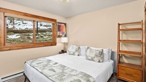 A bedroom with a large bed, a wooden shelf, a window with a view of a snowy landscape, and a poster on the wall.