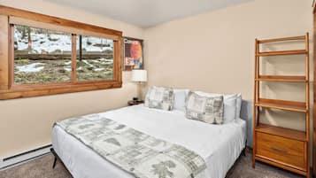 Een slaapkamer met een groot bed, een houten plank, een raam met uitzicht op een besneeerd landschap en een poster aan de muur.