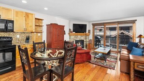 A spacious living room with a fireplace, wooden flooring, and a large TV mounted above it.