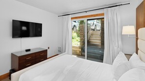 A bedroom with a bed, a TV, a dresser, and a sliding glass door leading to a balcony.
