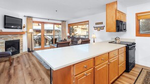 Une cuisine dotée d’un grand îlot central, de meubles en bois, d’une cuisinière noire et d’un téléviseur à écran plat fixé au-dessus de la cheminée.