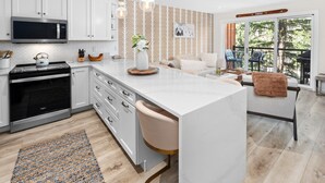 A modern kitchen with white cabinetry, a large island, and a dining area with a view. - Crestwood 2202 Premier 2 Bedroom (Snowmass Village)