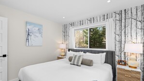 A bedroom with a large bed, a window with curtains, a nightstand with a lamp, and a wall-mounted painting. - Crestwood 2202 Premier 2 Bedroom (Snowmass Village)