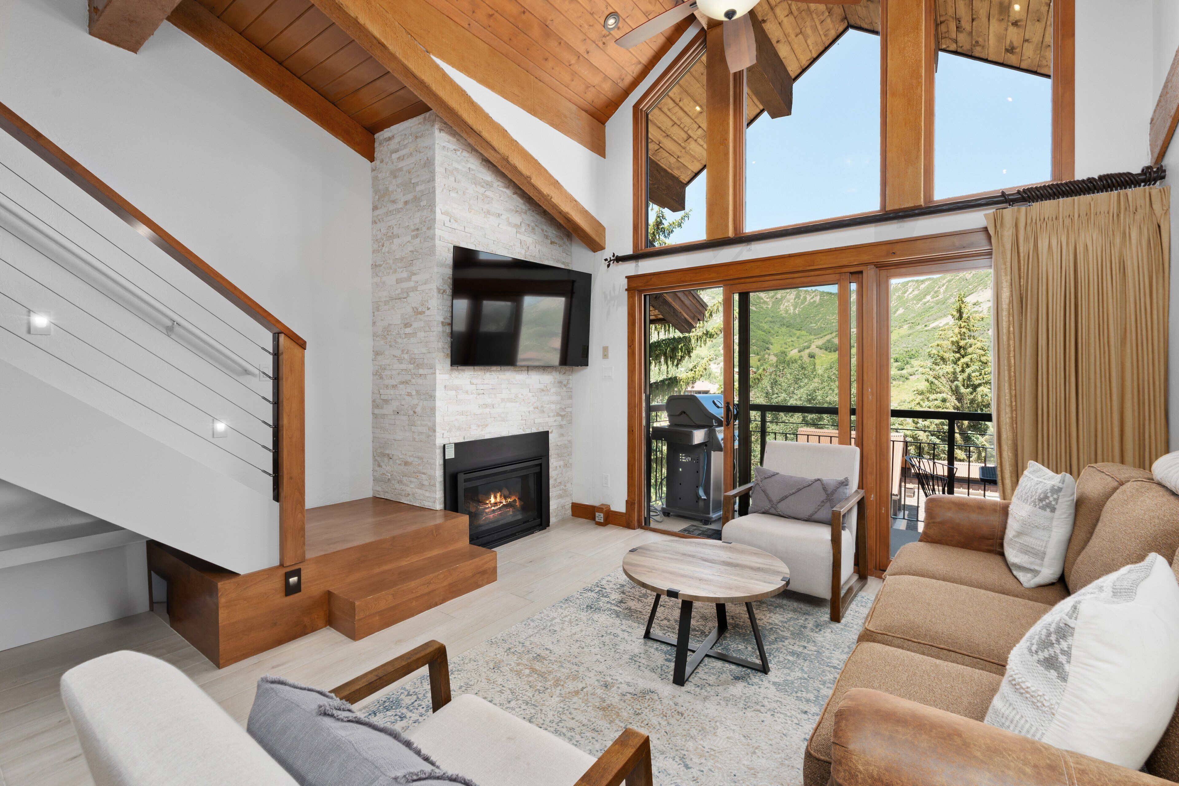 A spacious living room with a fireplace, a staircase, and a large window overlooking a scenic view.
