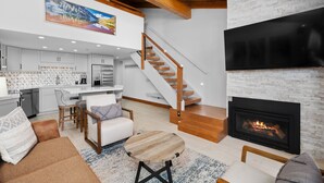Ein modernes Wohnzimmer mit Kamin, eine Küche mit weißen Schränken und eine Treppe, die in ein Obergeschoss führt.