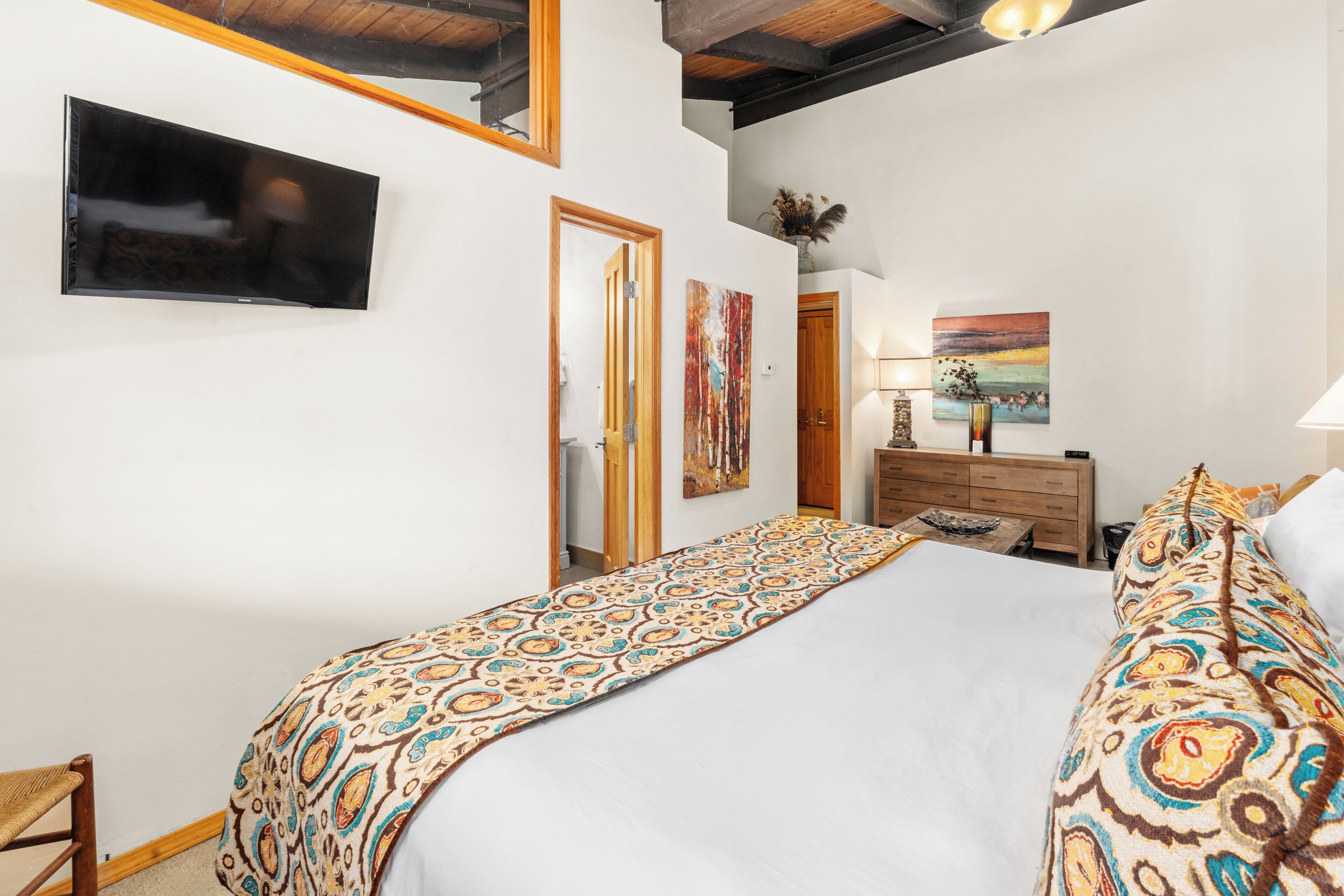 Une chambre à coucher avec un grand lit, une tête de lit en bois, une table de chevet, une commode et un téléviseur fixé au mur.