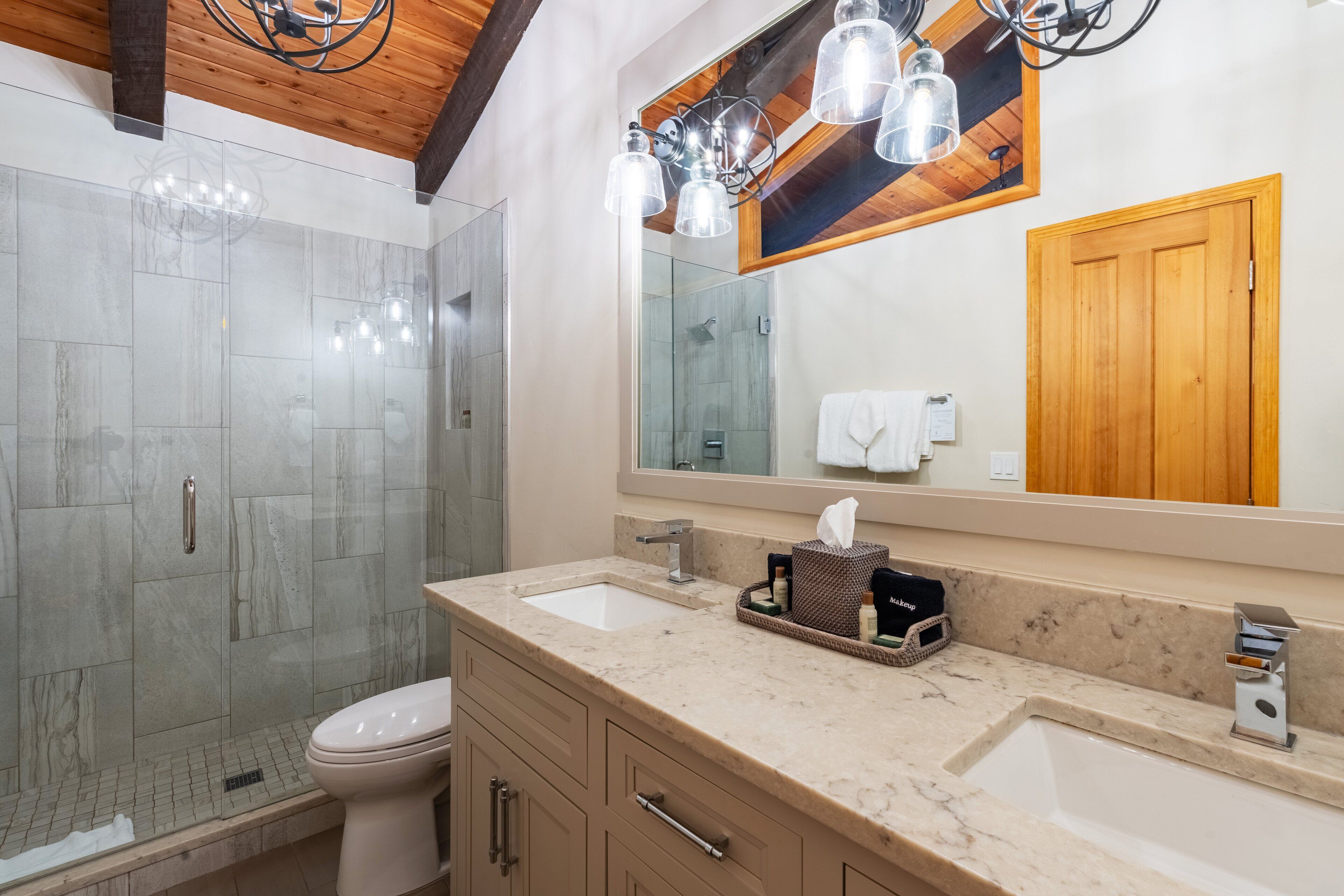 A modern bathroom with a glass shower enclosure, a double sink vanity, and a large mirror above the vanity.
