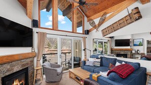 A spacious living area with a fireplace, comfortable seating, a television, and a large window overlooking a scenic outdoor area.