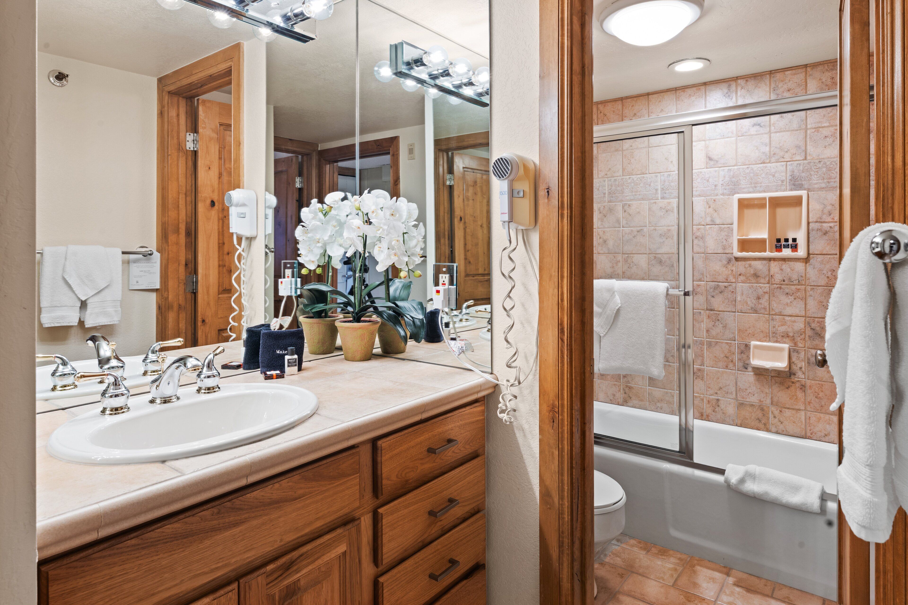 Un baño con tocador de madera, un espejo grande, un lavabo, ducha e inodoro.