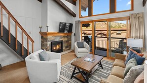 Un salón espacioso con chimenea, una escalera y un amplio ventanal corredera que da a un patio exterior.