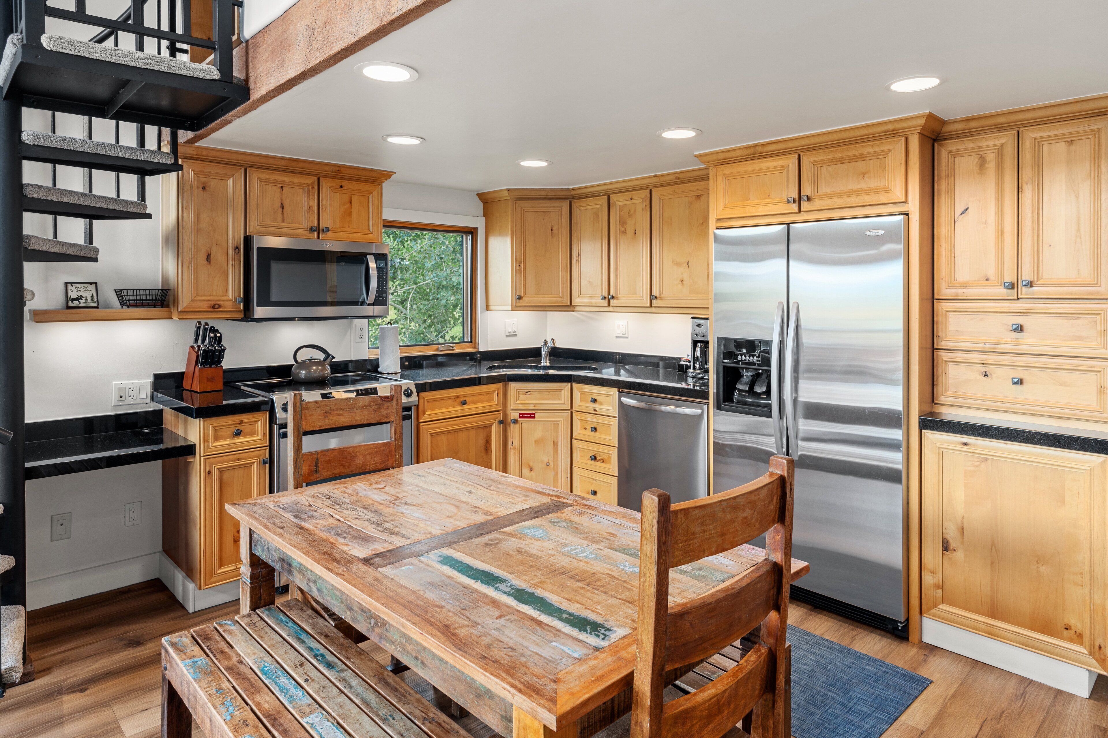 A modern kitchen with wooden cabinets, a stainless steel refrigerator, and a dining area with a rustic table and chairs.