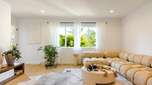 Una sala de estar moderna con un sofá color beige, una mesa redonda y un gran ventanal con cortinas.