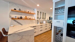 Una cocina moderna con encimeras de mármol, estantes de madera y un botellero.