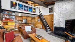 A spacious living area with a fireplace, a wooden staircase, and a loft with bookshelves and artwork. - Crestwood 3301 Deluxe 1 Bedroom Plus Loft (Snowmass Village)