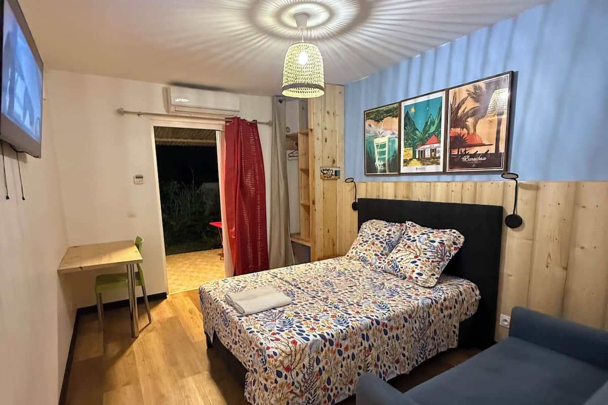 Un dormitorio con cama, escritorio, silla, sofá, una lámpara de techo y dos cuadros colgados en la pared.