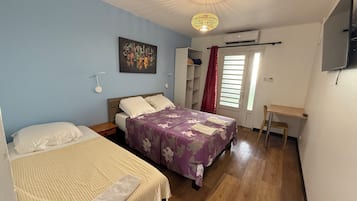 Ett sovrum med två sängar, ett skrivbord, en stol, en taklampa, ett fönster med gardiner och en väggmonterad TV.