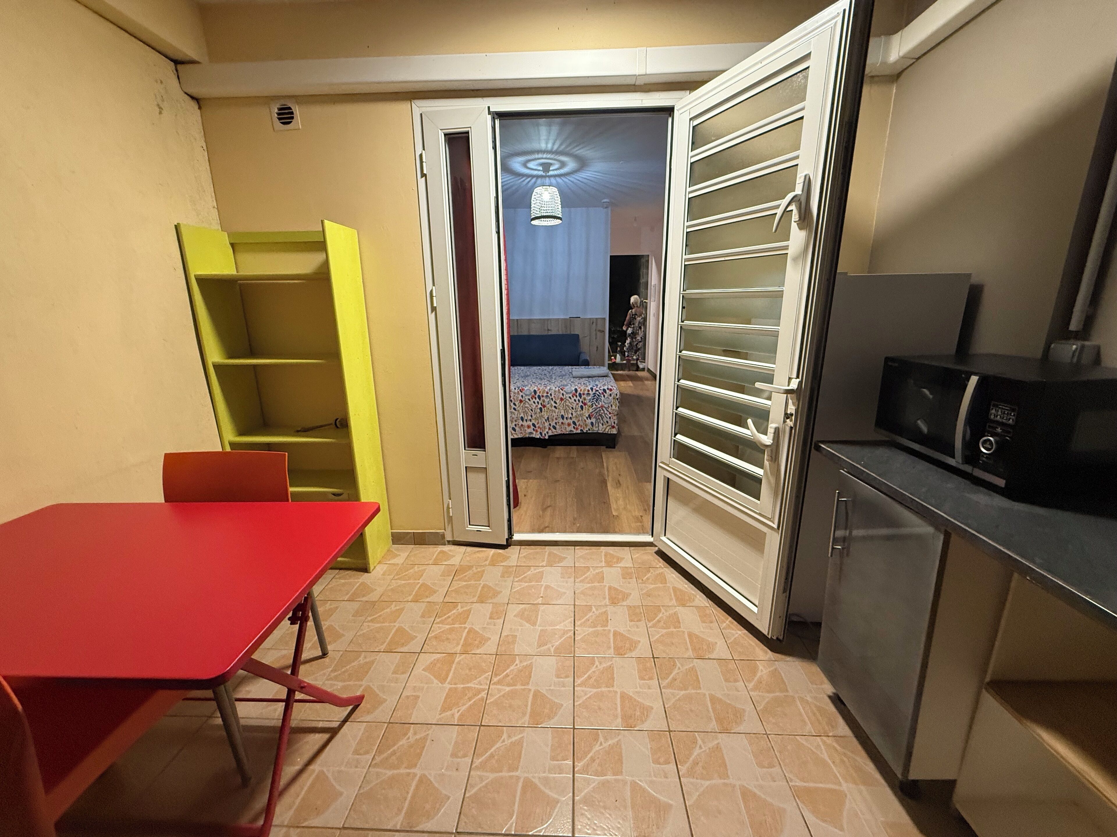 A compact kitchen with a red table, a yellow shelving unit, and a microwave.