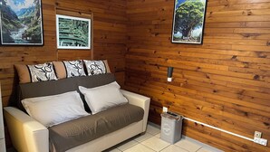 Ein Raum mit Holzwänden, einer Couch, zwei Wandbildern und einem Mülleimer.