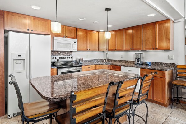 A kitchen with wooden cabinets, a granite countertop, a refrigerator, a microwave, an oven, and a sink.