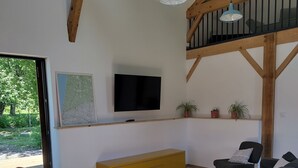 Ein modernes Wohnzimmer mit Holzboden, einem an der Wand befestigten Fernseher, einer Couch, einem Schaukelstuhl und einer Treppe.
