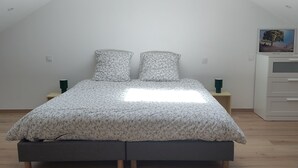 Ein Schlafzimmer mit schrägem Dach, einem Bett mit floralem Bettbezug, einem Nachttisch, einer Kommode und einem Gemälde an der Wand.