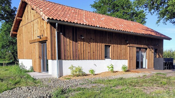 Ein Holzhaus mit rotem Ziegeldach, großen Türen und einer kleinen Veranda.