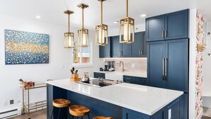 A modern kitchen with dark blue cabinets, a white island with stools, and pendant lighting.