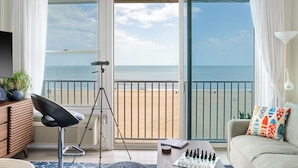 A room with a large sliding glass door to a beach, a tripod, a chessboard, and a sofa with colorful pillows. - Boardwalk Oceanfront Studio near Top Dining (Virginia Beach)