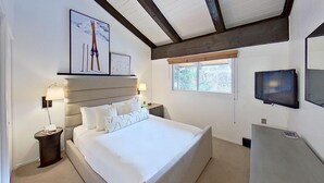 A bedroom with a large bed, two bedside tables, a TV, and framed pictures on the wall.