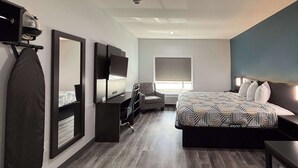 A modern hotel room with a large bed, a desk, a chair, a TV, and a wardrobe. - Studio 6 Dallas, TX – Fair Park (Dallas)