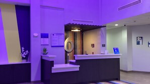 A reception area with a modern design, featuring a reception desk, a large number '6' sign, and a small plant on the counter. - Studio 6 Dallas, TX – Fair Park (Dallas)