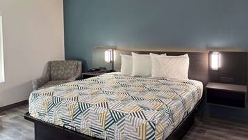 Una habitación de hotel moderna con una cama grande, una mesita de noche, una silla y una lámpara fijada en la pared.