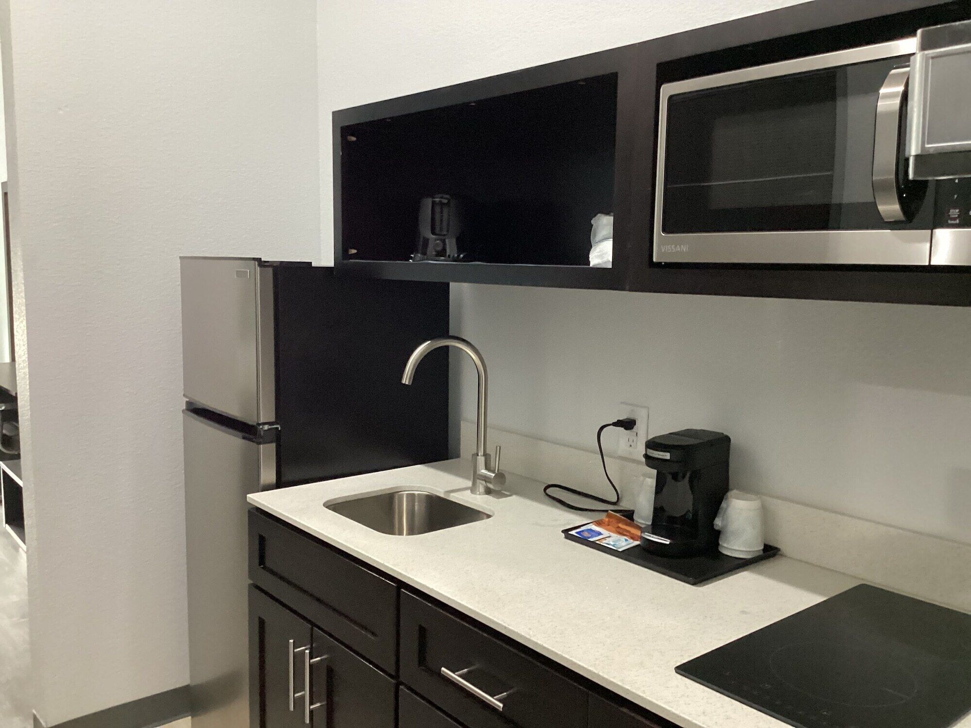 A compact kitchen with a stainless steel refrigerator, a microwave, a coffee maker, and a sink.