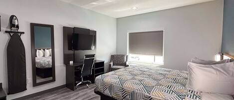 A modern bedroom with a large bed, a desk, a chair, a television, and a window with a view.