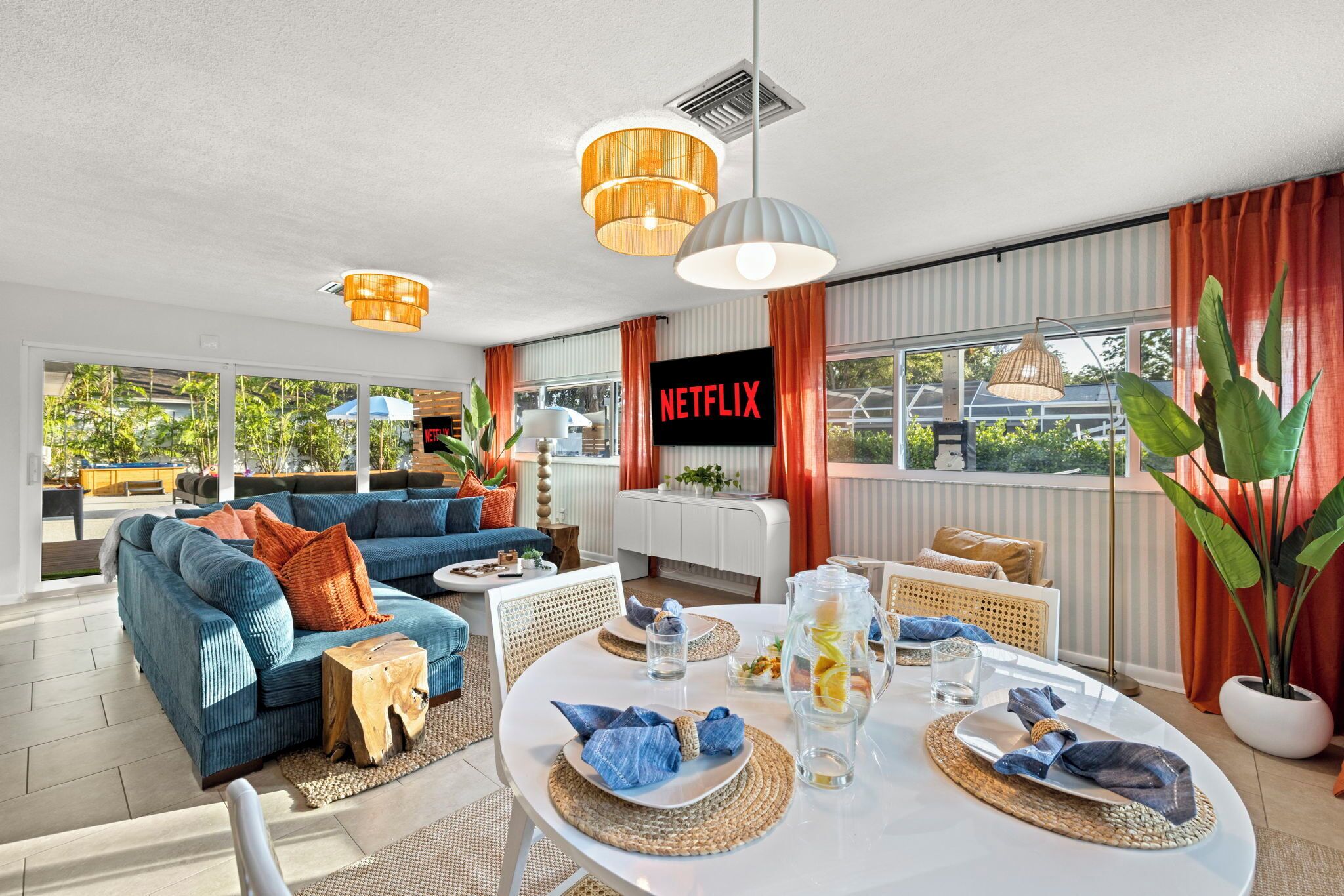 A modern living room with a blue sofa, a dining table set for four, and a large window with curtains.