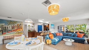 A modern living room with a blue sofa, white dining table, and a kitchen in the background.